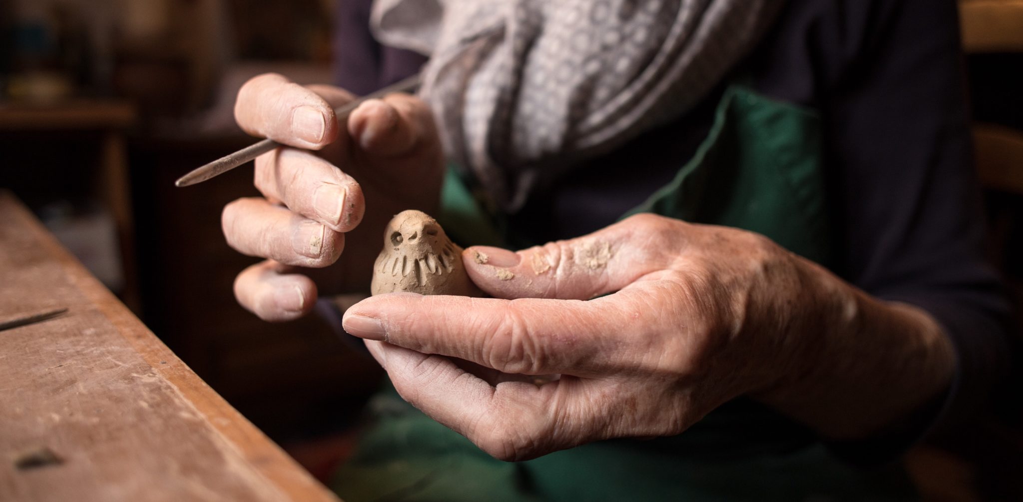 a pair of elderly hands carving a bird in clay